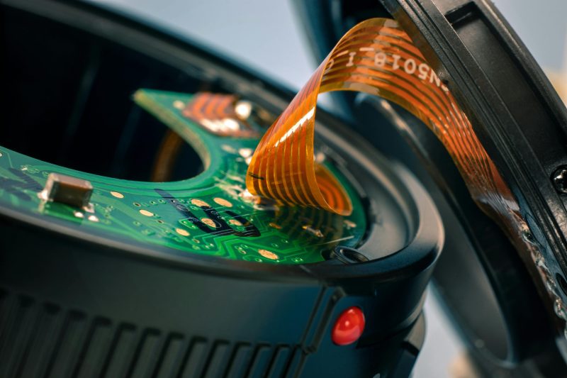 Detailed close-up of circuit board and ribbon cable in a disassembled camera lens.